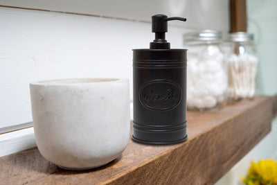 Autumn Alley Matte Black Farmhouse Metal Soap Dispenser on bathroom shelf. The stylized 'Wash' label and embossing stand out.